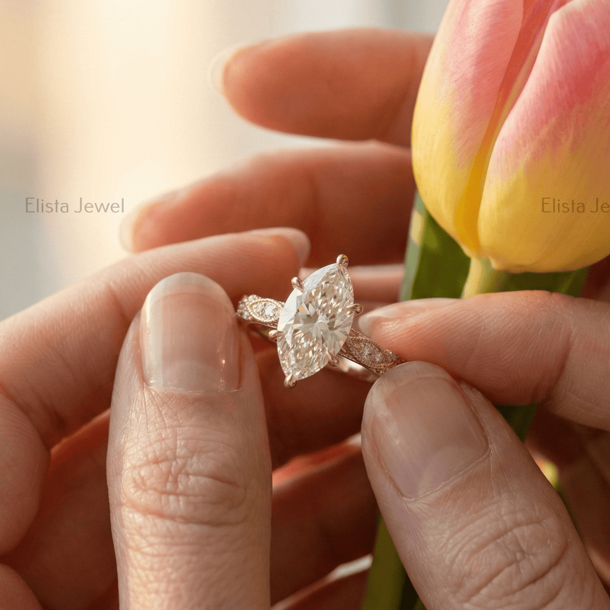 Close-up of a hand holding a diamond ring with a blurred background featuring a tulip.